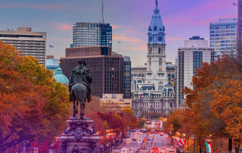 Philadelphia cityscape with equestrian statue in foreground and ornate city hall in background amidst autumn trees.